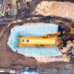 Aerial view of construction site with a large yellow underground storage tank and workers, surrounded by excavation equipment.